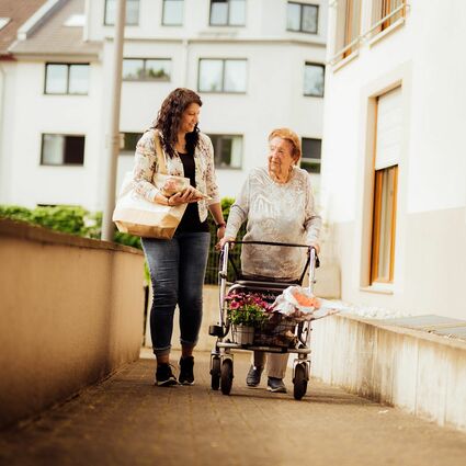 Junge Frau geht mit älter Frau und Rollator spazieren