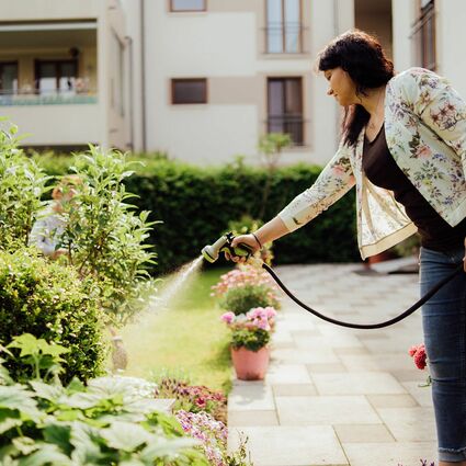 Junge Dame gießt mit Wasserschlauch den Rasen
