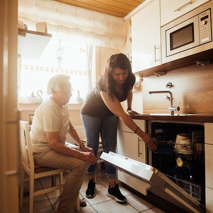 Junge Dame hilft älteren Dame beim ausräumen der Spühlmaschine
