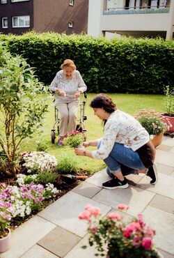 Seniorenbetreuer pflanzt Blumen bei der Gartenhilfe ein