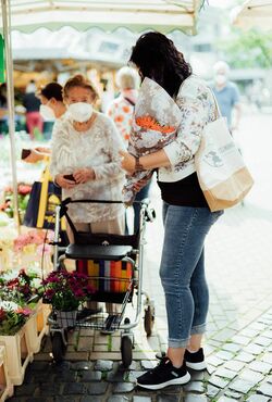 Seniorin und Seniorenbetreuerin kaufen auf dem Markt ein